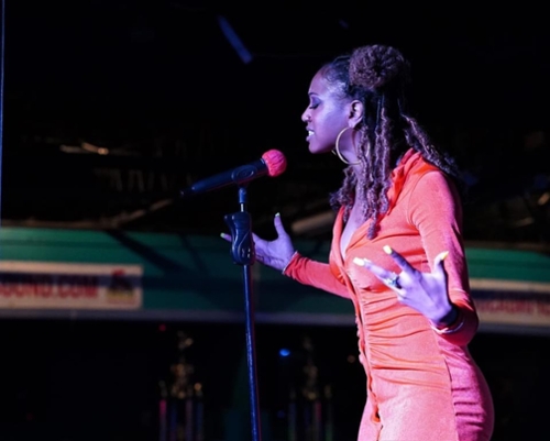 A black woman singing into a micrphone wearing red clothing.