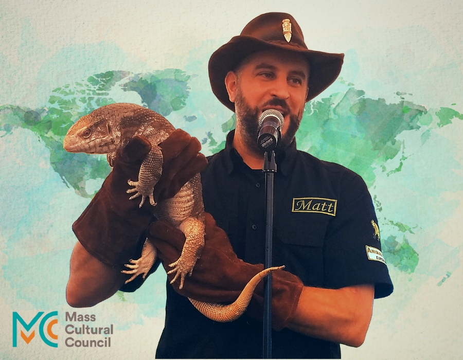 A man in a brown ranger hat wearing large brown gloves and holding a large lizard.